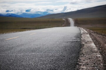 Road through fields leading to snowy mountains, sunny day