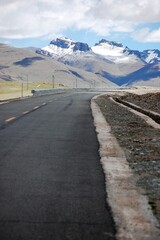 Road through fields leading to sunlit and snowy mountains, cloudy sky background