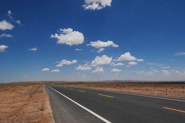 Naklejka premium Isolated desert highway stretching out into the horizon, surrounded by lush clouds