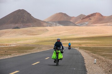 Obraz premium Human riding bicycle on road through desert surrounded by mountains