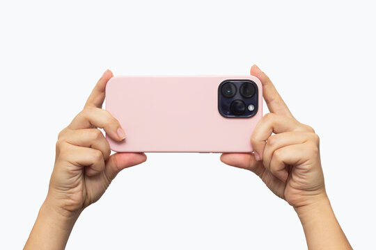 Mobile phone with photo camera in a pink case in female hands isolated on a white background. Blank with an empty copy space for the design. Mockup of a smartphone. Young woman takes picture