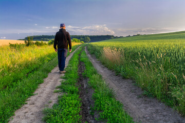 A man in a black hooded sweatshirt walks along a country road between fields