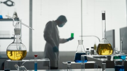 Laboratory of modern medical research. A male scientist analyzes a green liquid in a flask. Blurred...