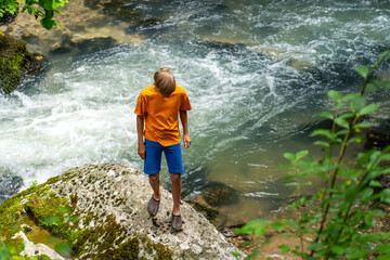 Boy stands on a stone on the bank of a stormy mountain river