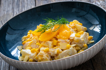 Fruit salad - peaches, pineapples, almonds and corn in mayonnaise on wooden table