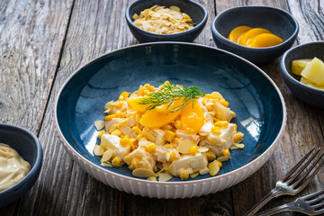 Fruit salad - peaches, pineapples, almonds and corn in mayonnaise on wooden table