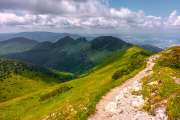 View of the vast mountains in Mala Fatra National Park, Slovakia, on a hot day of summer with cloudy sky. Summer hiking in the mountains. Green and blue colors. Hiking trail on the ridge.