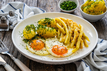Summer dinner - sunny side up eggs, boiled yellow beans and prepared potatoes served on wooden table
