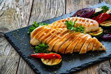 Grilled chicken breast and vegetables on wooden table
