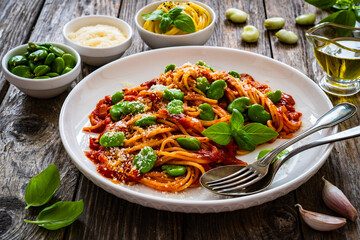 Spaghetti in tomato sauce with broad bean, parmesan cheese and basil leaves on wooden table