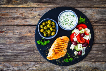 Grilled chicken breast and Greek salad on wooden table 