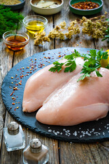Fresh raw chicken breasts on cutting board with spices on wooden background
