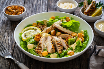 Caesar salad - fried chicken breast and vegetables on wooden table
