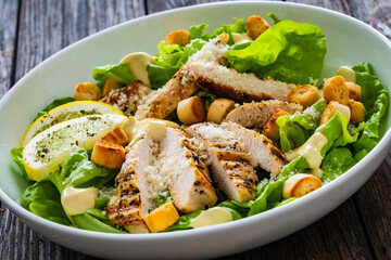 Caesar salad - fried chicken breast and vegetables on wooden table
