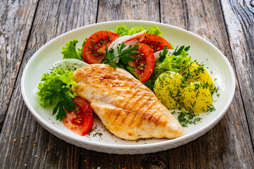Grilled chicken breast, boiled potatoes and fresh vegetables on wooden table
