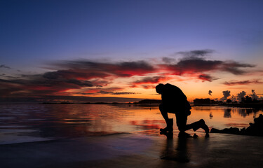 Man Kneeling In Prayer By Reflection Water Sunset