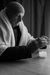 Portrait of a freezing old man at home without heating warming his hands over a candle, no heating...