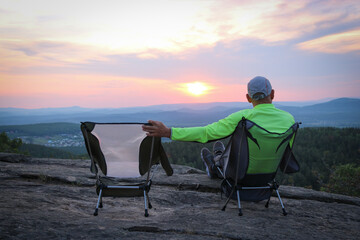 A lonely man admires the sunset and hugs an empty chair. The concept of loneliness and loss. - 619055820