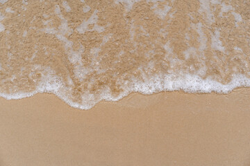 closed up of sea wave with white foam and softness sand background textured on a sunny day, clean...