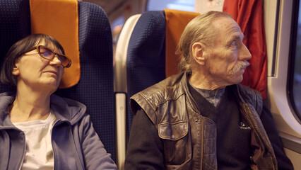 An elderly couple is travels in train, senior looks at out the window, a woman sleeping
