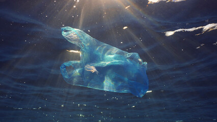 Disposable blue plastic bag floats under surface in blue water in sunrays. Plastic bag thrown into...