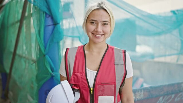 Young beautiful hispanic woman architect smiling confident holding hardhat at street