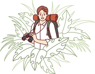 Man traveler stands in thickets of jungle and holds binoculars exploring area in search further path
