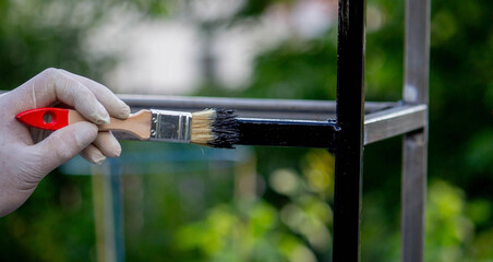 a man paints metal with black paint with a brush.