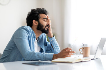Tired Indian Male Feeling Sleepy While Sitting At Desk In Home Office