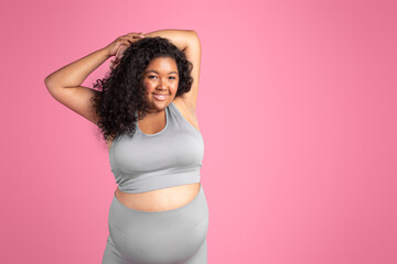 Smiling african american plus size woman doing arm stretching exercise, training on pink background, free space
