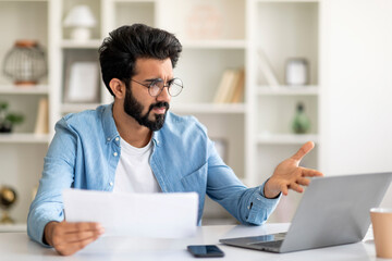 Stressed young indian man working with papers and laptop at home office