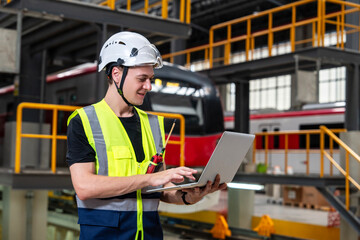 Caucasian man in uniform and helmet holding tablet looking at checklist checklist and doing electric train maintenance report in electric train depot