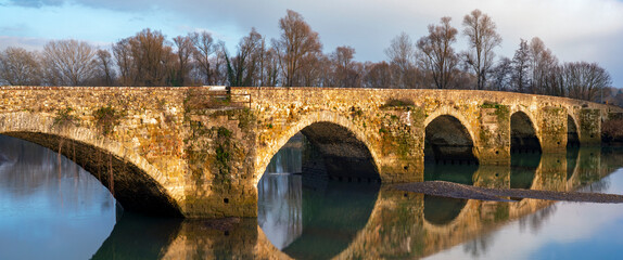 Fototapeta premium Picturesque Ponte Buriano in Arezzo, Italy is reflected beautifully in the calm waters of the river