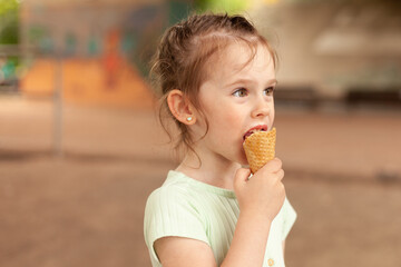 Cute blonde girl in a dress eats an ice cream cone outdoors