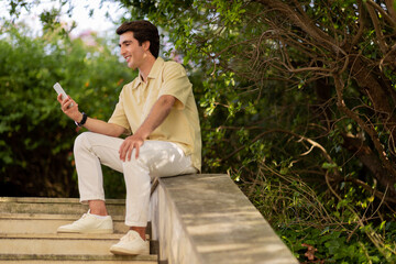 Fototapeta premium relaxed handsome guy sitting on stairs outdoors, using phone