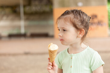 Cute blonde girl in a dress eats an ice cream cone outdoors