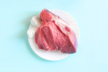 A piece of raw red meat with onion slices on a white plate on a light background close-up