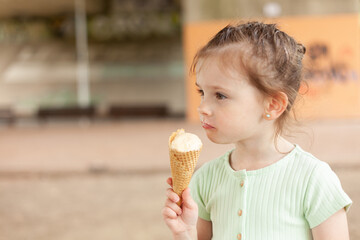 Little blonde girl in a dress eats an ice cream cone outdoors