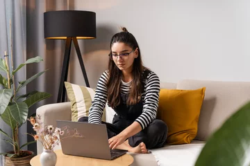 Fototapete Musikladen Charming focused multi-ethnic woman with glasses working on laptop from home in cozy room