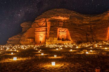 Starlight sky over the ancient nabataean tombs of Mada'in Salih Hegra city illuminated, night panorama, Al Ula, Saudi Arabia