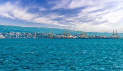 cargo sea port with cranes vehicles, container stacks , supplies and trucks with goods, sea hub terminal from seashore