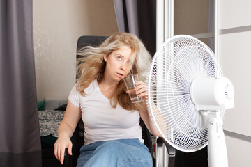 Tired woman seeking relief from high temperatures, trying to cool down in a non-air-conditioned...
