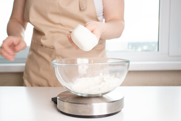 weight for baking recipes, woman weighing flour in a plate on a digital kitchen scales