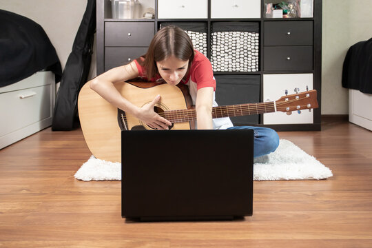 teenager girl playing guitar at home, Young musician practicing guitar with a laptop computer