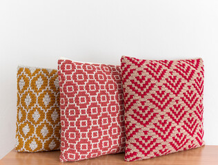 Soft crochet pillows on a wooden table against white wall. Handmade crochet pillows with abstract mosaic pattern. Copy space.