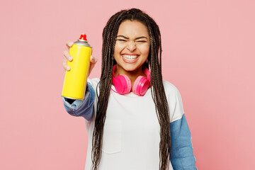 Young woman of African American ethnicity in white sweatshirt casual clothes hold in hand container with spray paint for graffiti stretch hand to camera isolated on plain pastel light pink background.