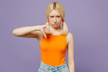 Young displeased dissatisfied sad blonde woman she wear orange tank shirt casual clothes showing thumb down dislike gesture isolated on plain pastel light purple background studio. Lifestyle concept.