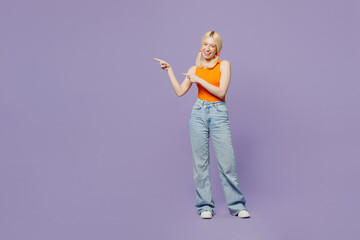 Full body young blonde woman wear orange tank shirt casual clothes point index finger aside indicate on workspace area copy space mock up isolated on plain pastel purple background. Lifestyle concept.