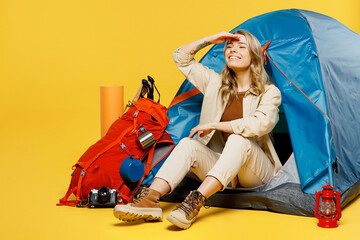 Full body fun young woman sit near bag with stuff tent look aside far away isolated on plain yellow...