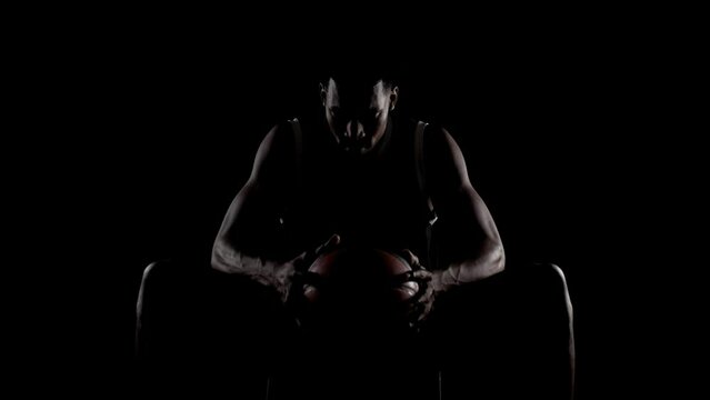 Basketball player sitting on a bench. Concentrated african american sports man against black background.